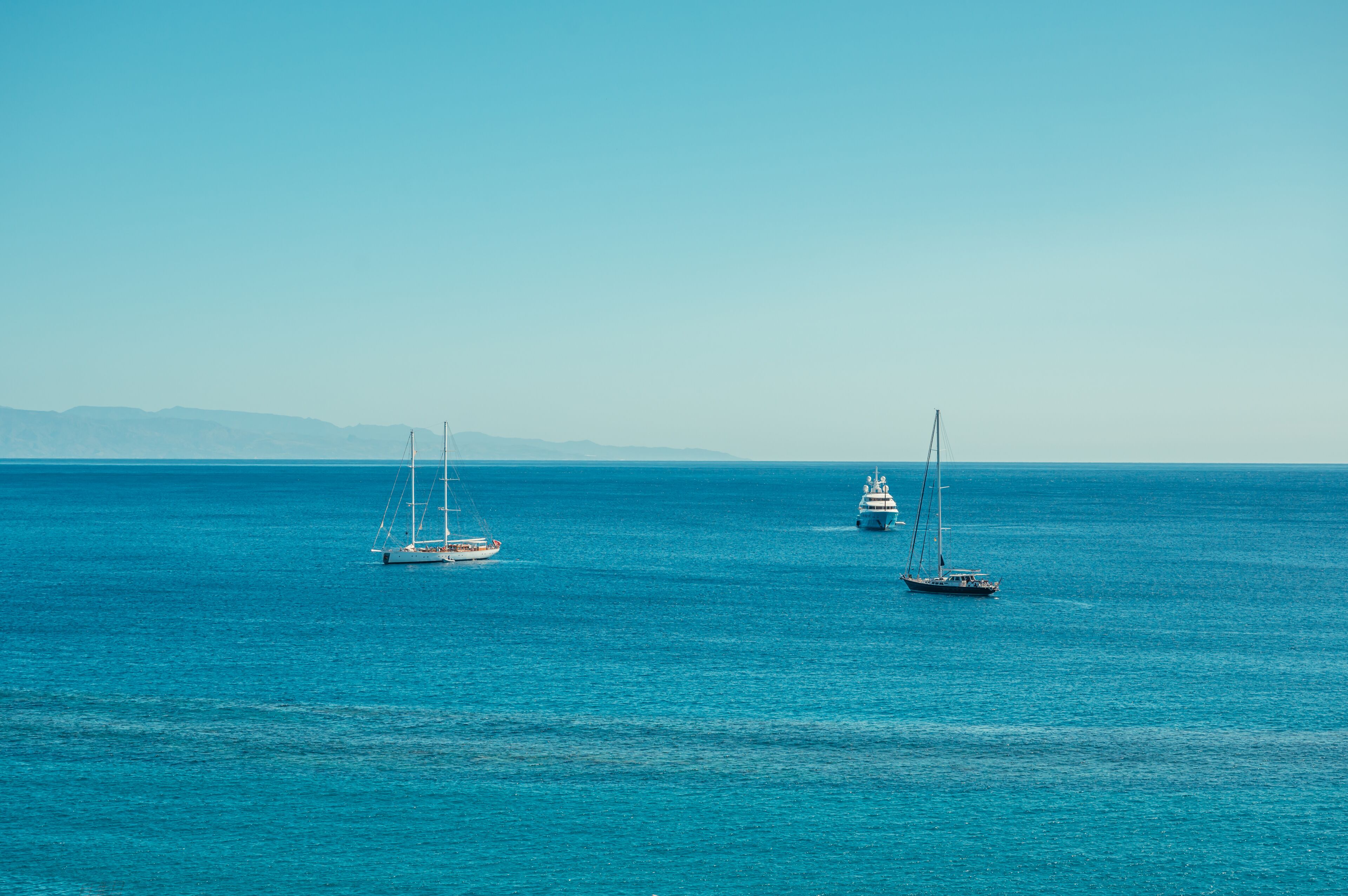 A calm sea with three sailboats.
