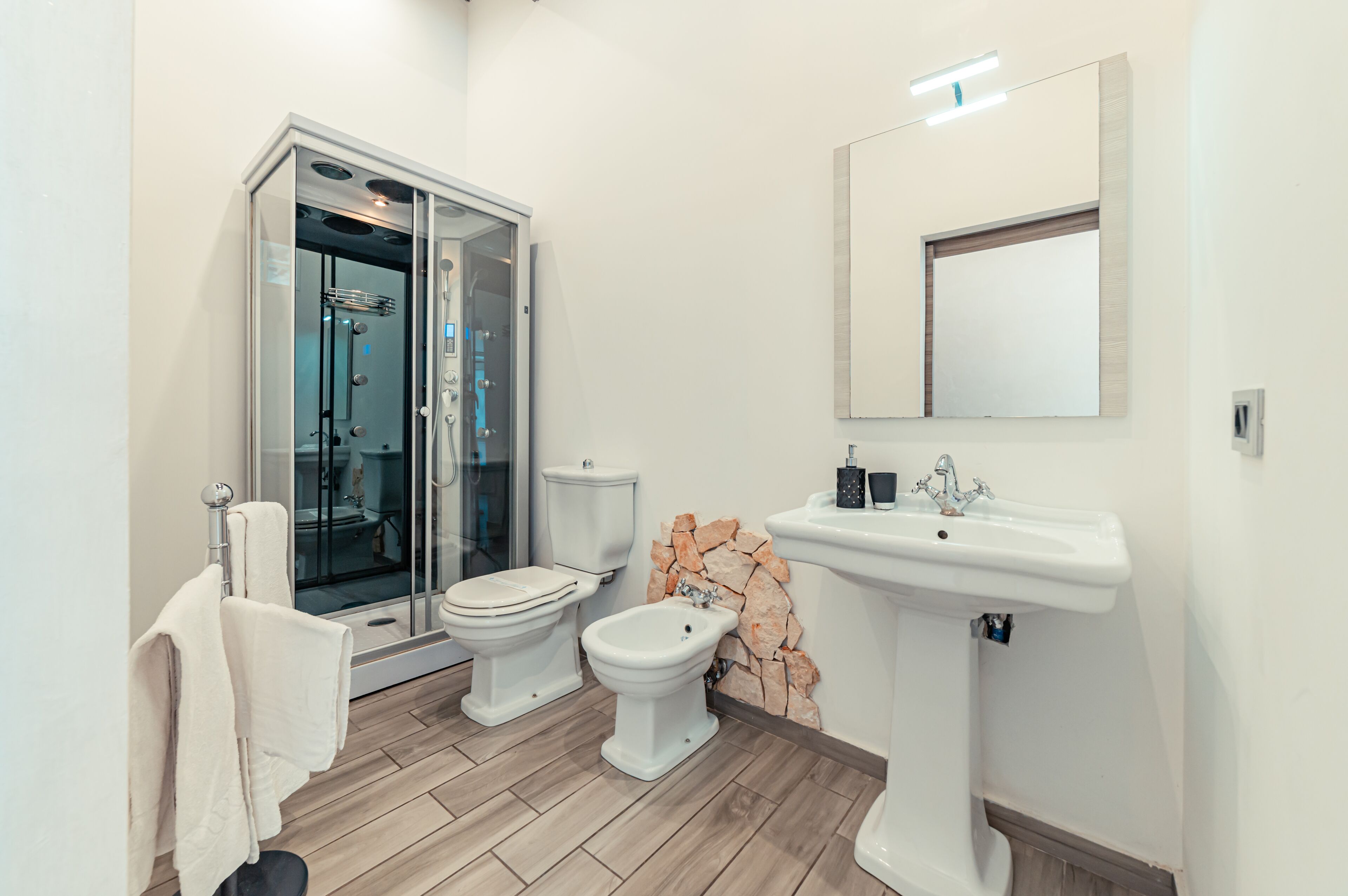 Un baño moderno con ducha de vidrio, inodoro, bidé y lavamanos sobre pedestal.