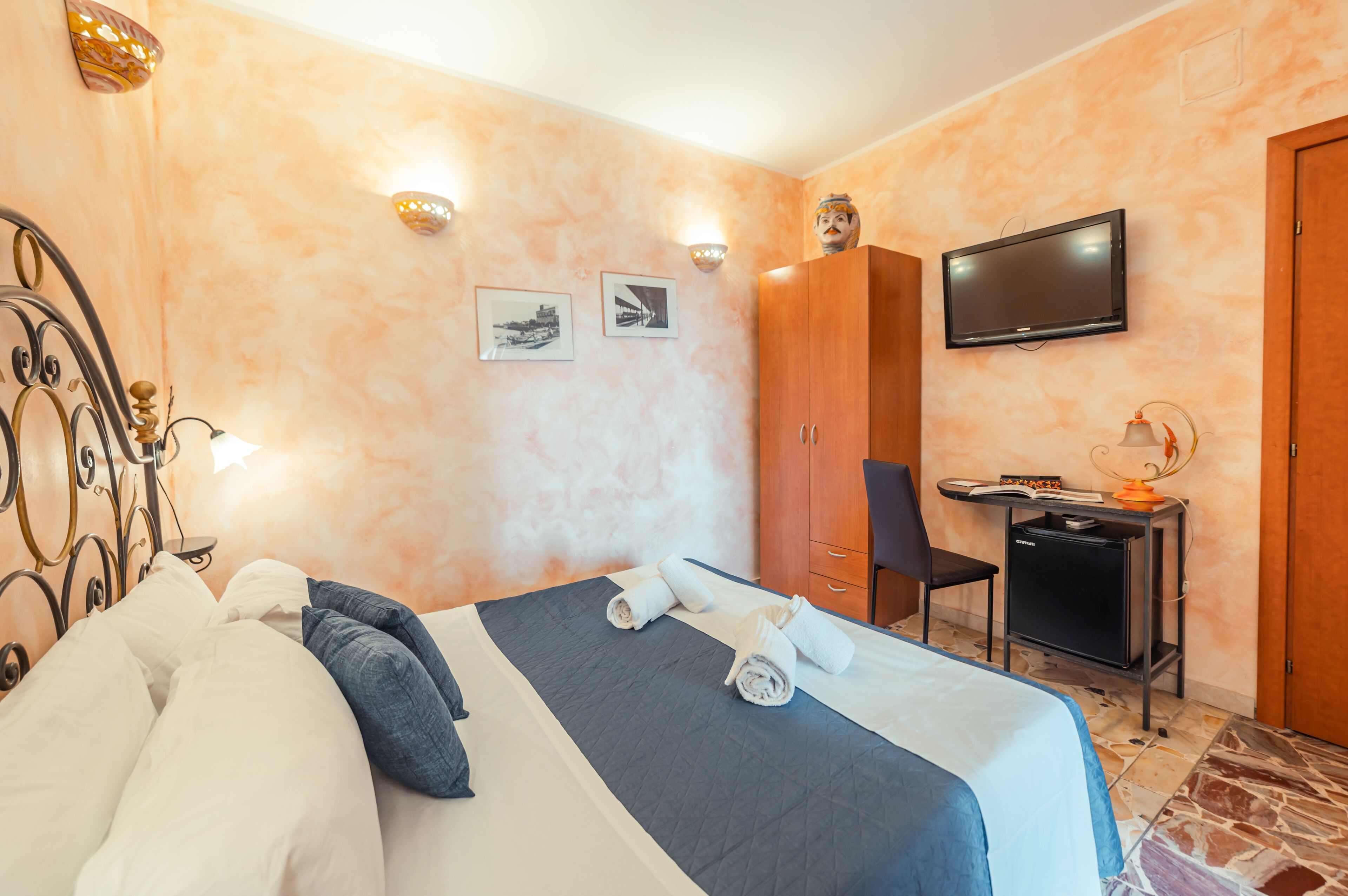 Una habitación de hotel con una cama, un escritorio con computadora, televisión y armario.