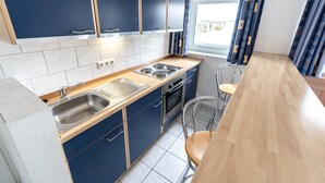 A modern kitchen with blue cabinets, a stainless steel sink, and a wooden countertop. - Hotel Fresh INN (Unterhaching)