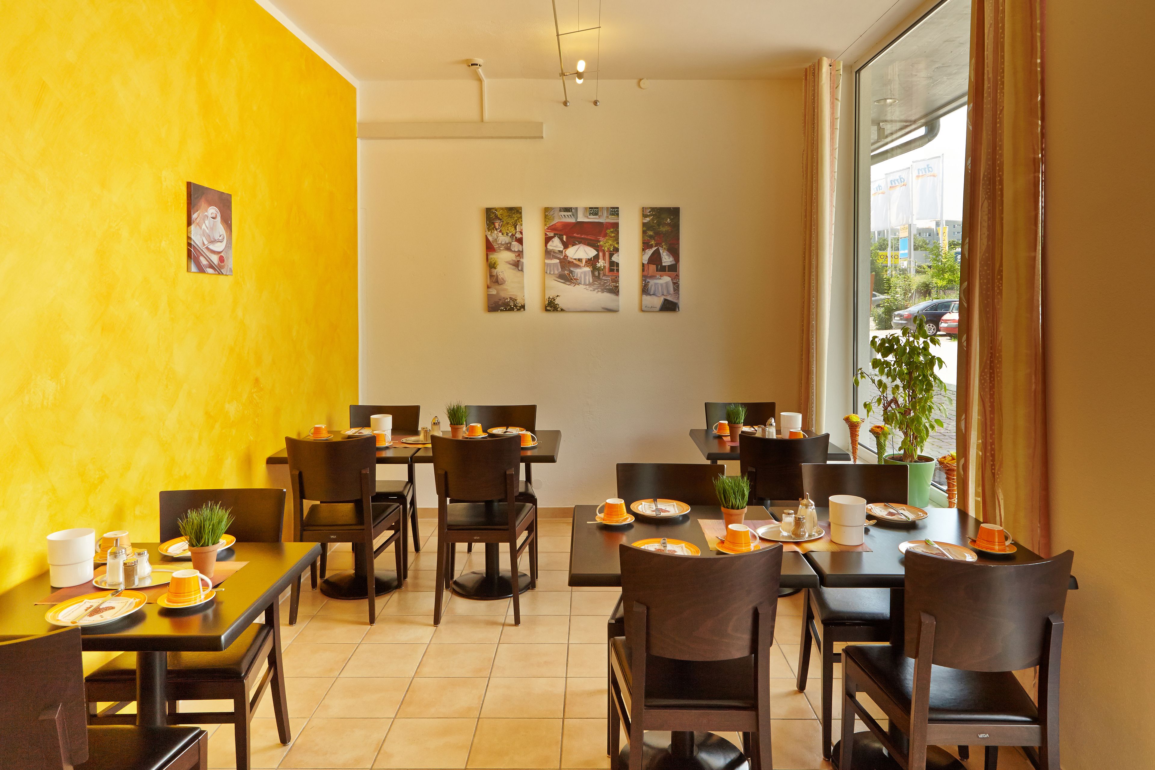 A dining area with tables and chairs, a yellow wall, and a window with a view of the outside.