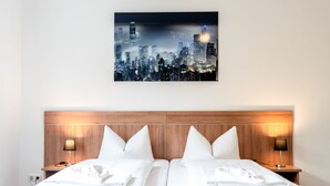 A hotel room with a cityscape view, a wooden headboard, two beds with white linens, and bedside lamps. - Hotel Fresh INN (Unterhaching)