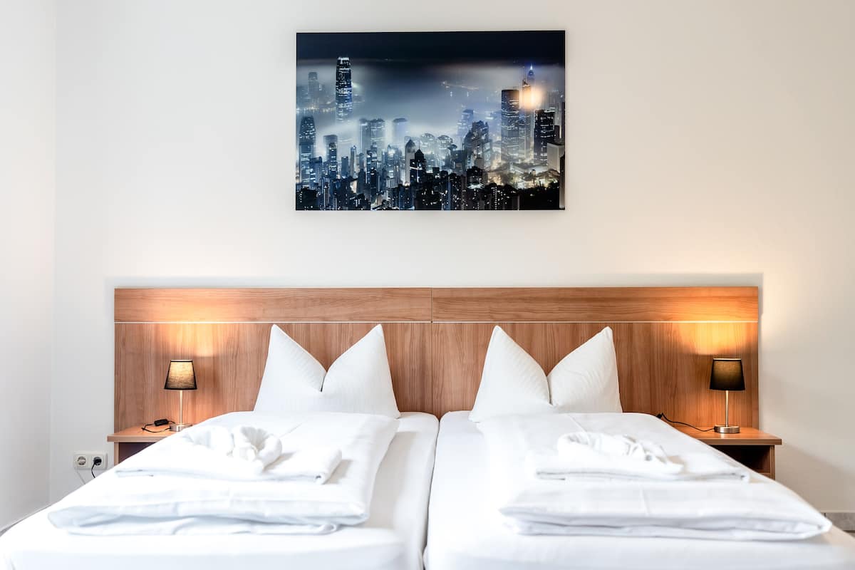 A hotel room with a cityscape view, a wooden headboard, two beds with white linens, and bedside lamps.