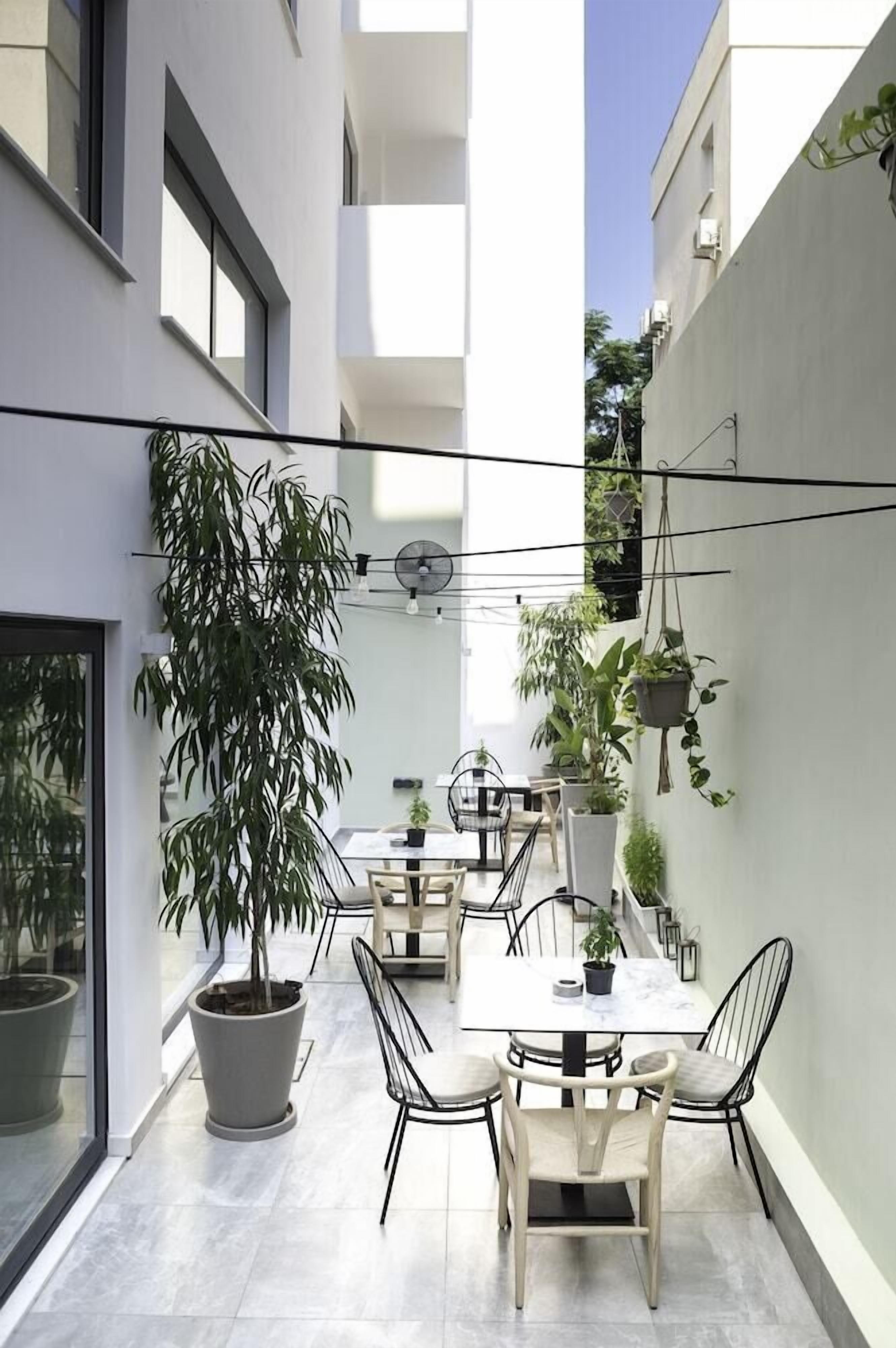 A modern outdoor dining area with a table and chairs, surrounded by potted plants and a clear sky.