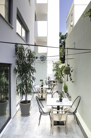 A modern outdoor dining area with a table and chairs, surrounded by potted plants and a clear sky. - Alexia Hotel Apts (Larnaca)