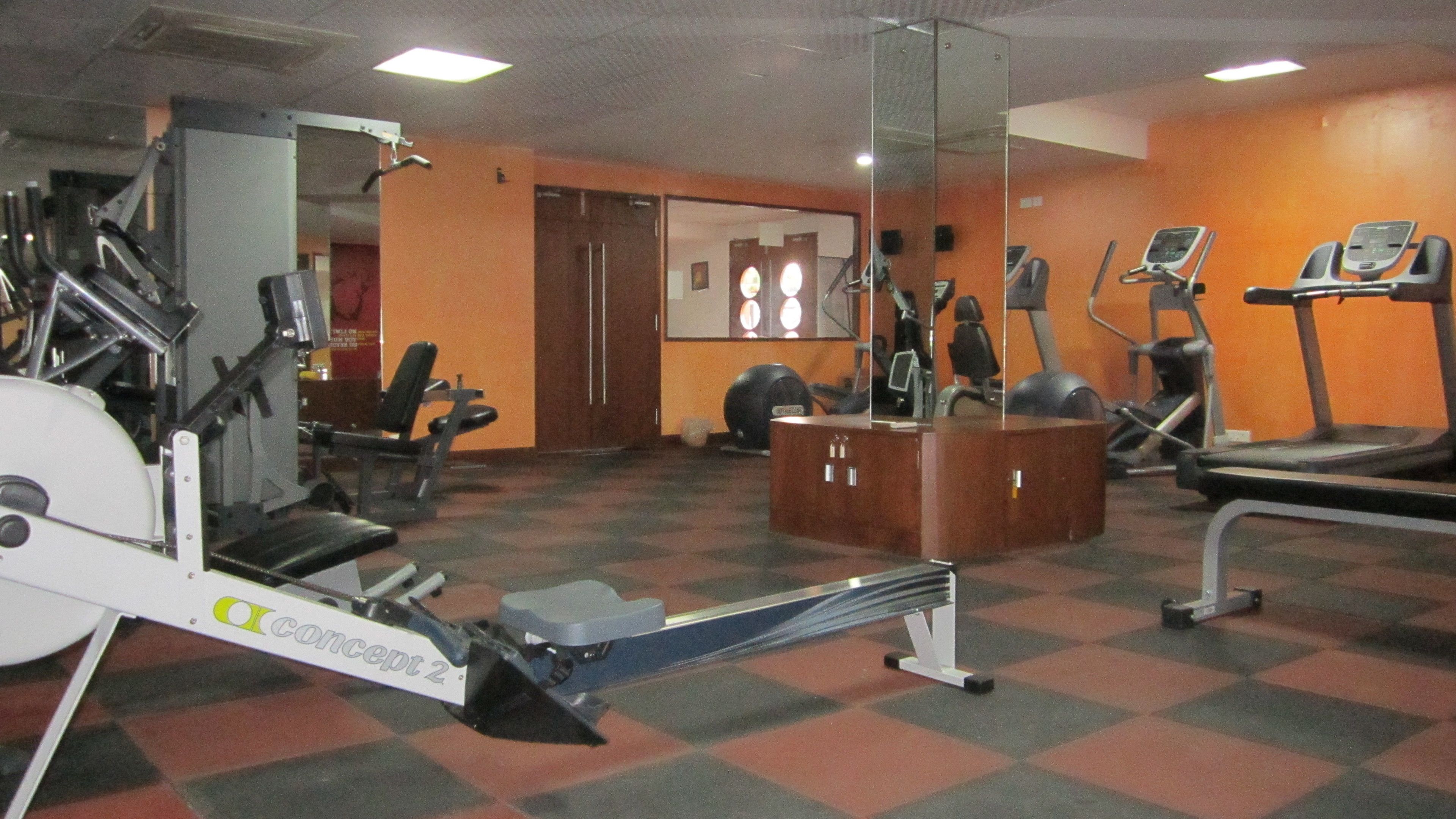 Academia com máquinas de cardio, equipamentos de musculação e um espelho grande.