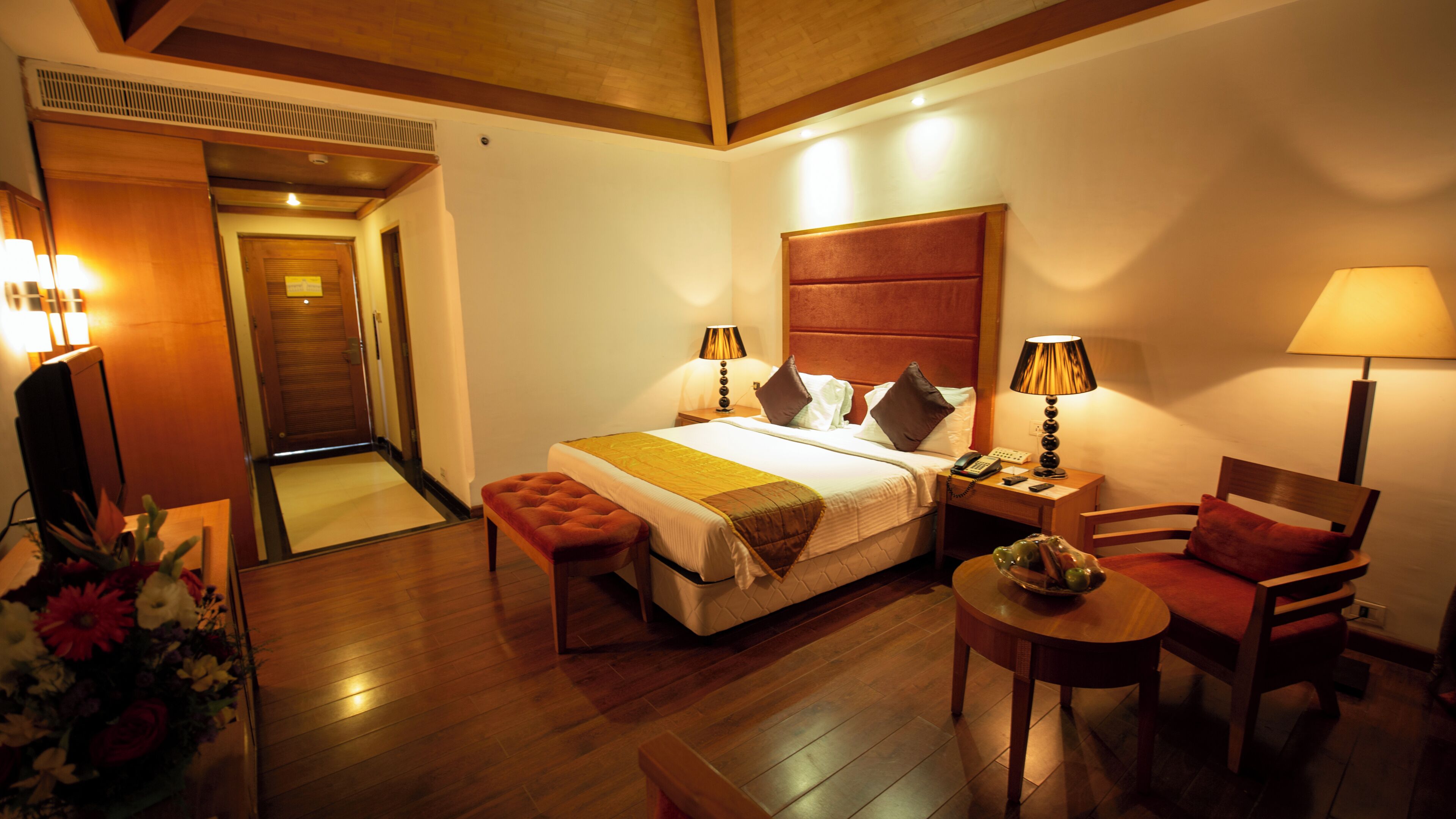 A hotel room with a bed, bedside tables, a desk, a chair, and a small table with a lamp.