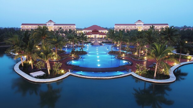 Ein Resort mit großem zentralen Pool, Palmen und einem Gebäude mit rotem Dach.