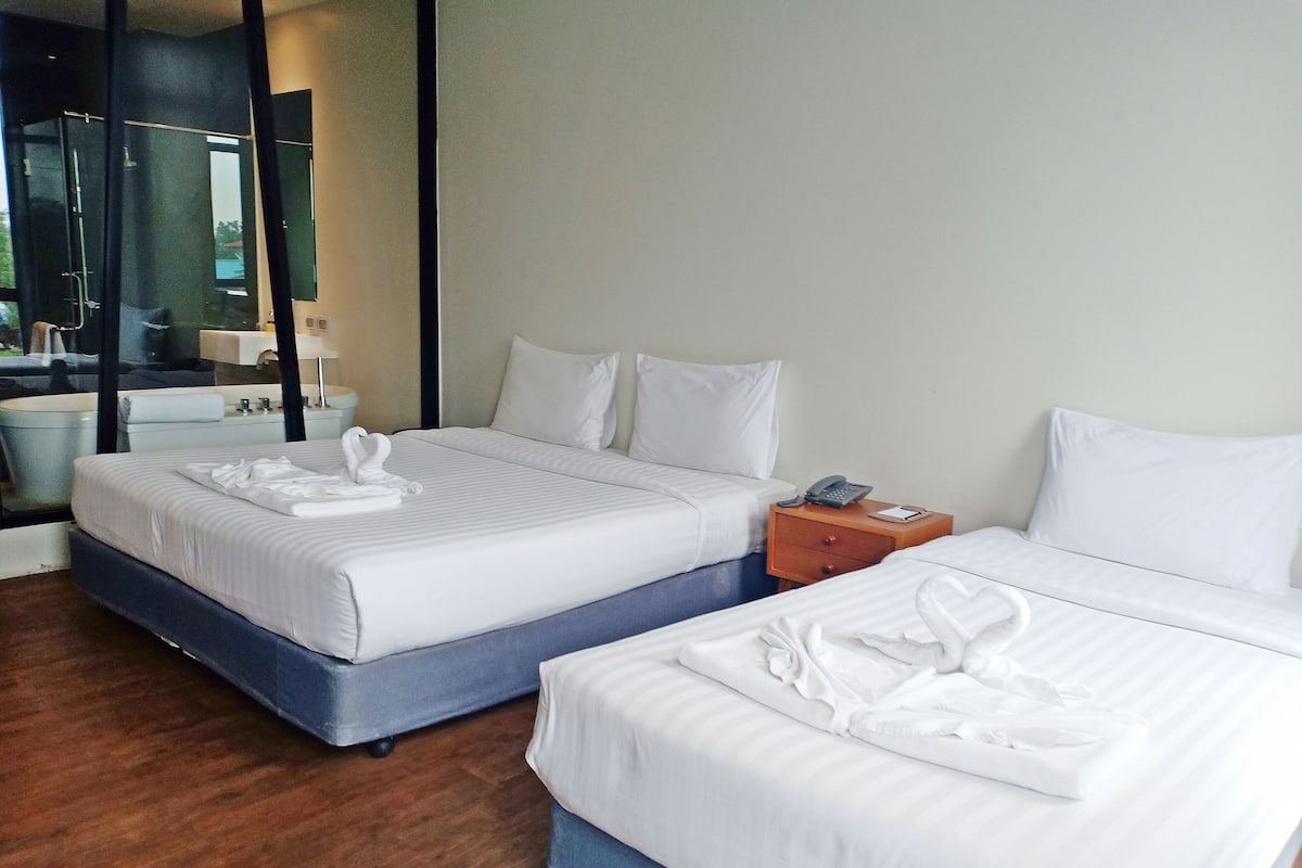 A hotel room with two beds, a wooden nightstand, a bathroom with a mirror, and a shower area.