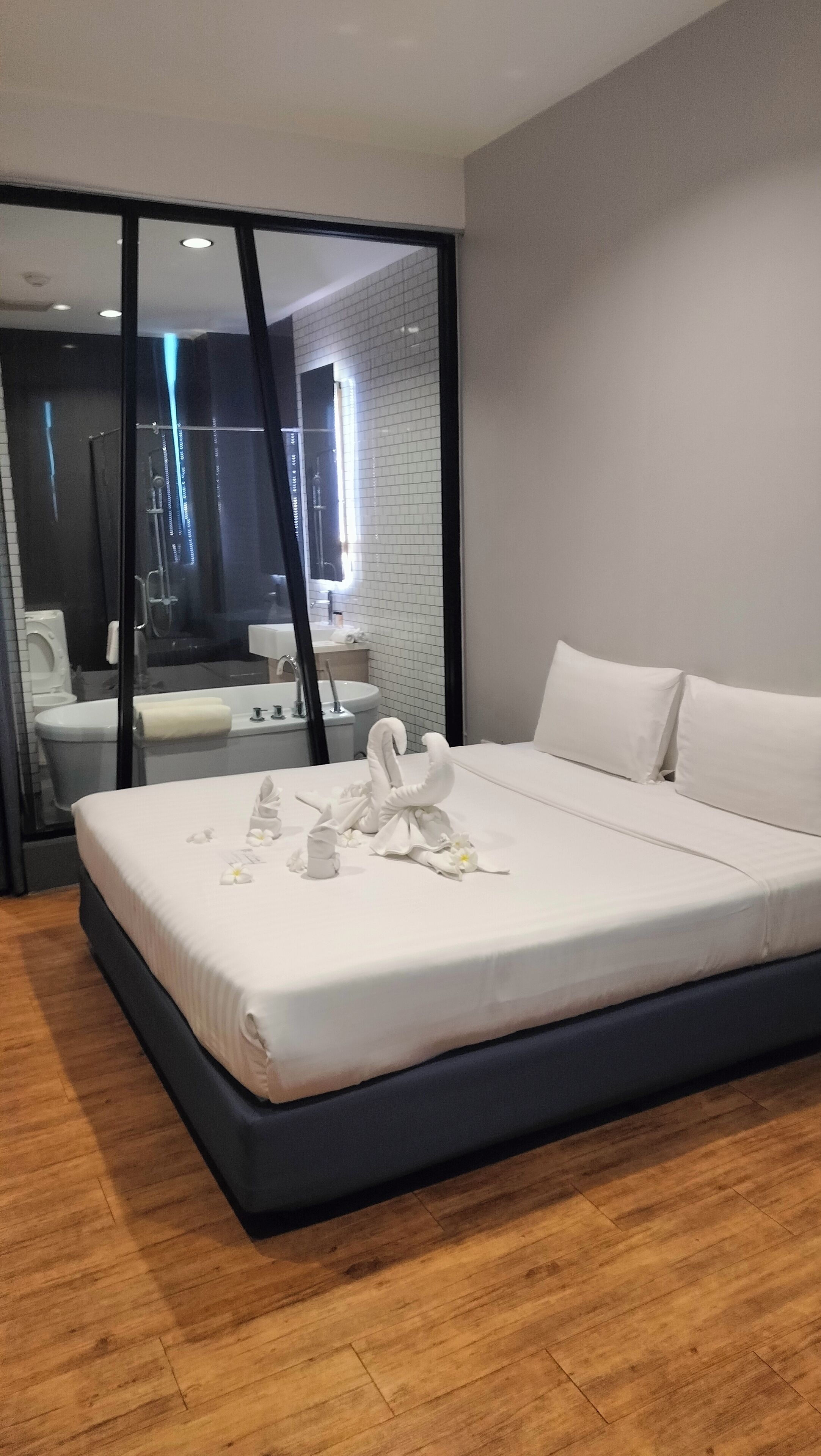 Une chambre d’hôtel moderne dotée d’un grand lit, d’une salle de bain avec une douche à parois de verre et offrant une vue sur le paysage urbain.