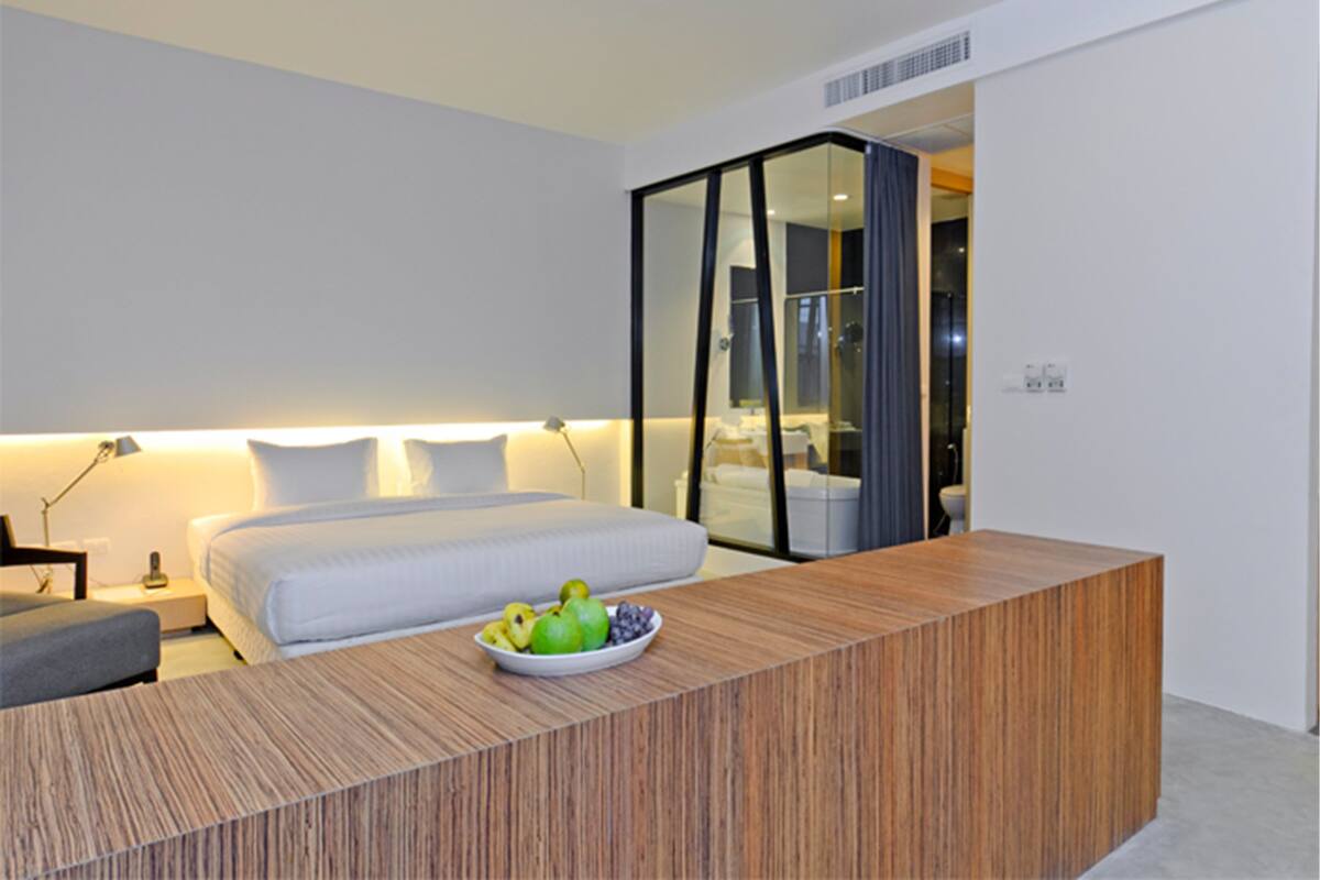 A modern hotel room with a large bed, a wooden desk, and a fruit bowl.
