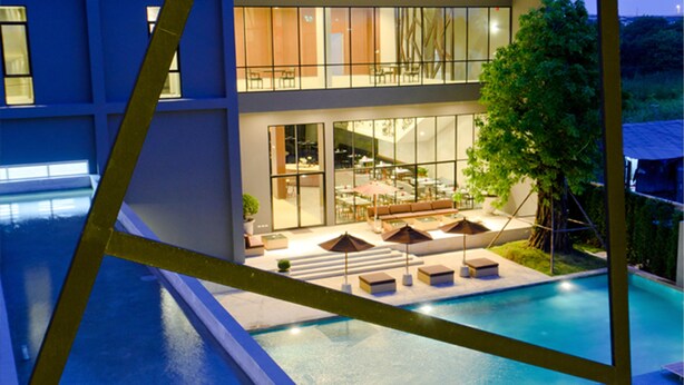 A modern building with a swimming pool, outdoor seating area, and a large glass facade. - Vismaya Suvarnabhumi Hotel (Bang Phli)