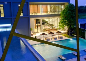 Un edificio moderno con piscina, zona de estar al aire libre y un amplio frente de cristal.