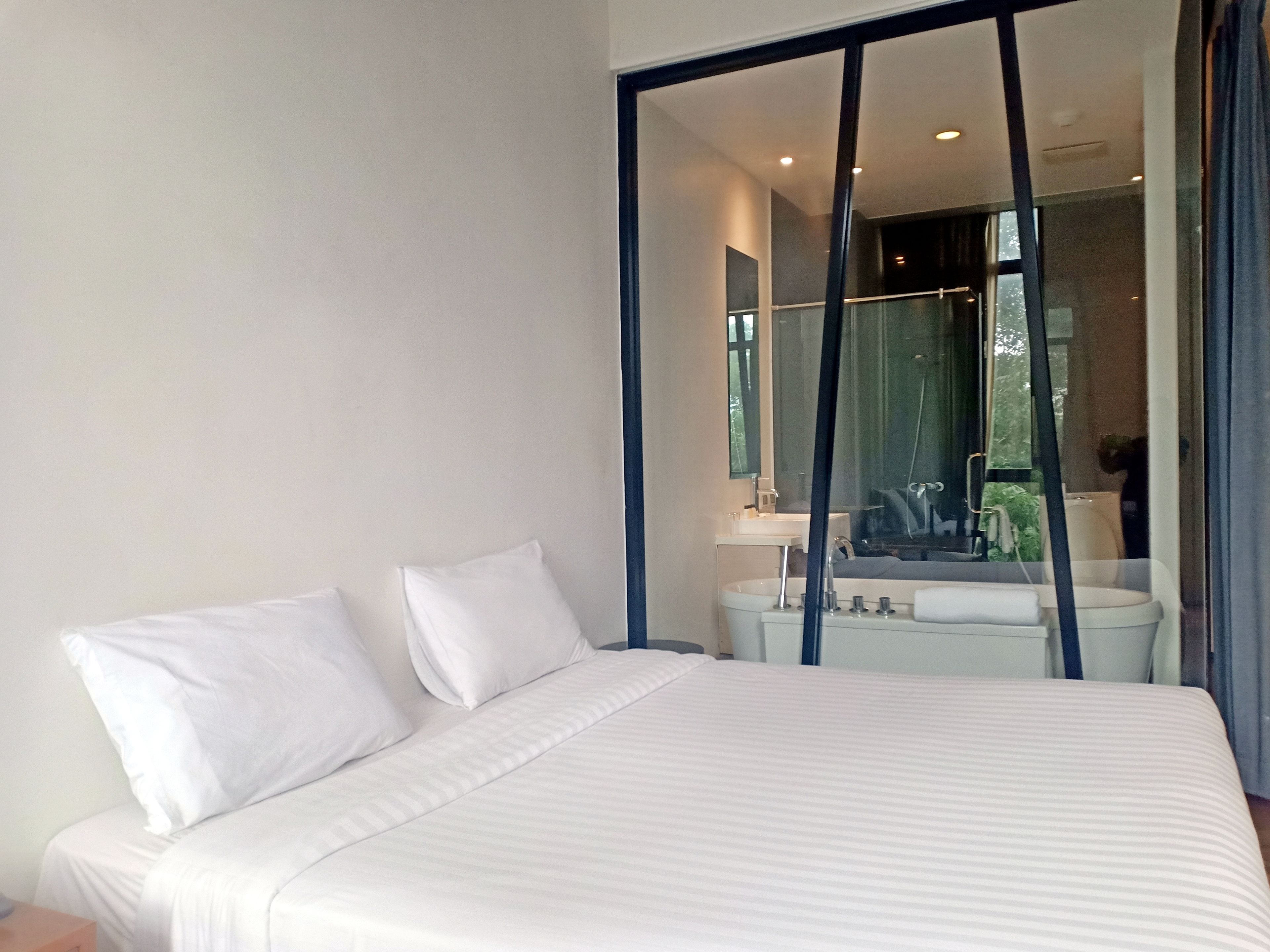A modern bedroom with a large bed, a bedside table, and a bathroom visible through a glass door.