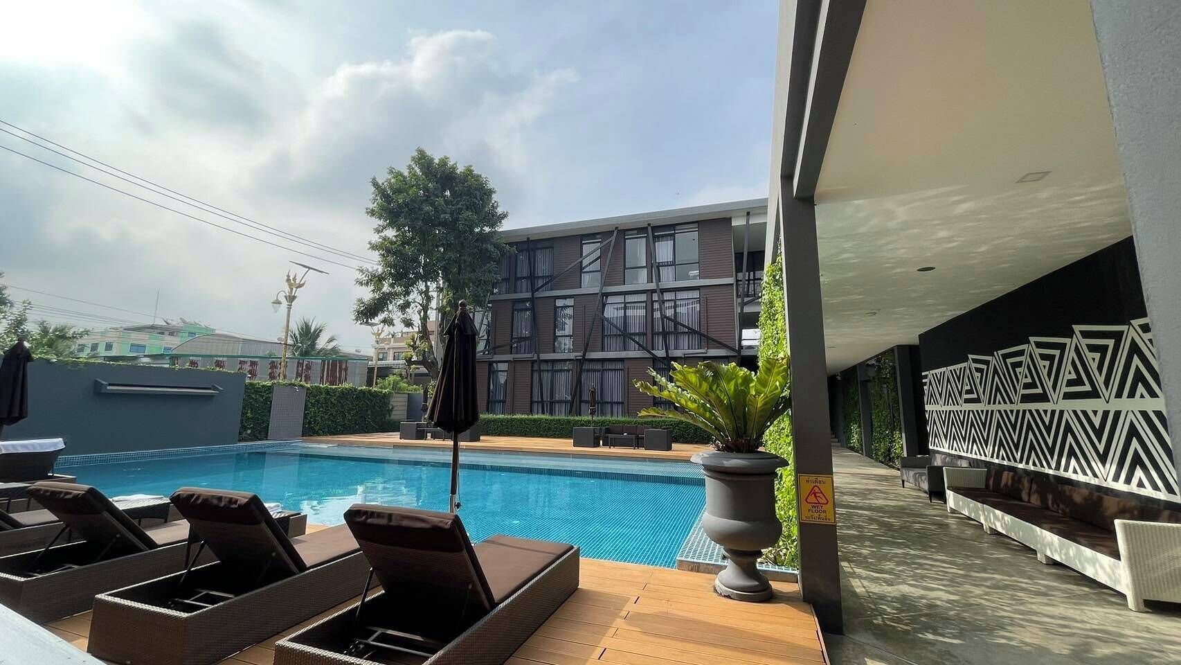 Un espace aménagé au bord de la piscine, avec des chaises longues, une piscine et un bâtiment moderne en arrière-plan.
