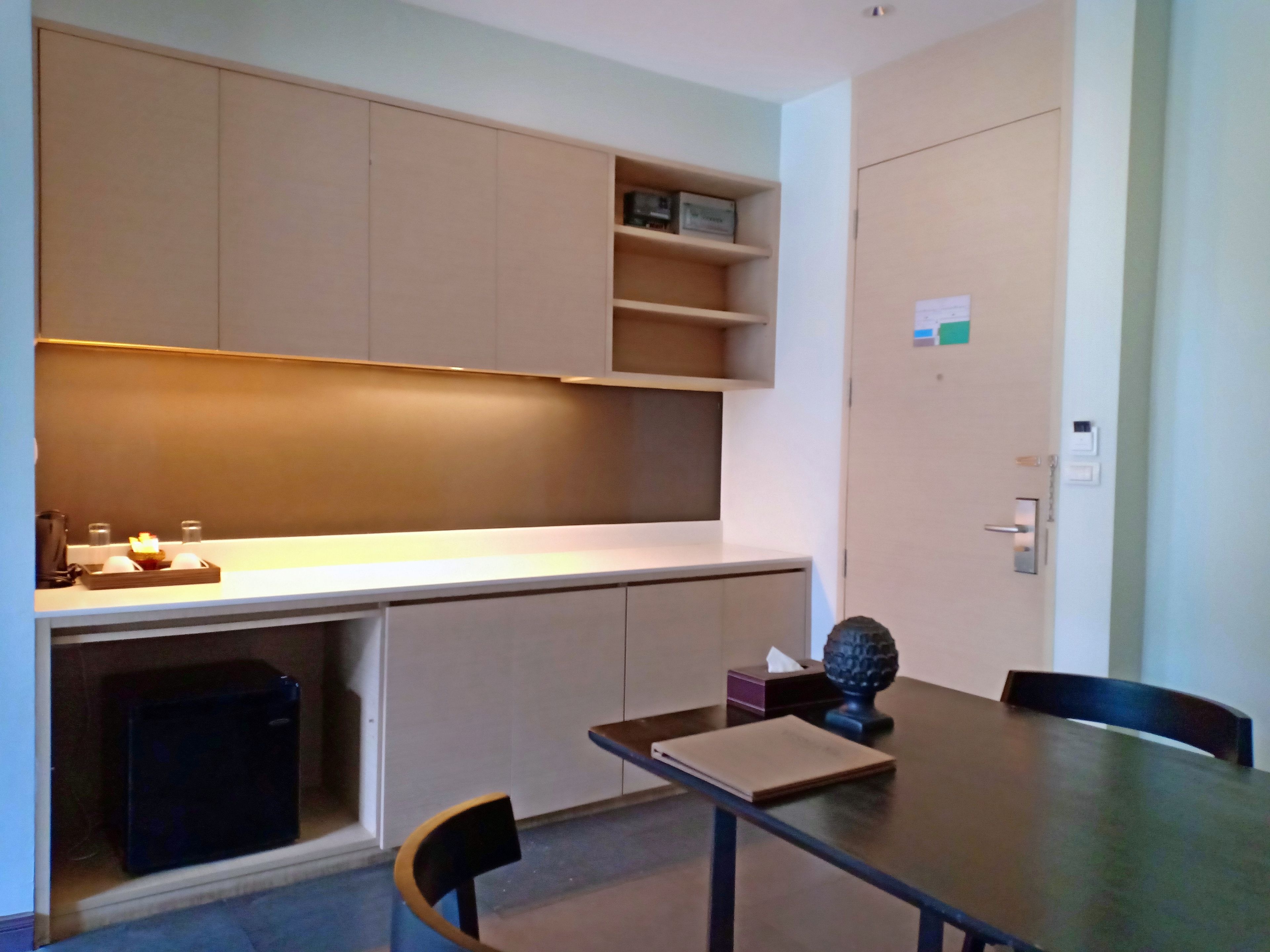 A modern room with a desk, chairs, a small trash bin, and a shelf with items.