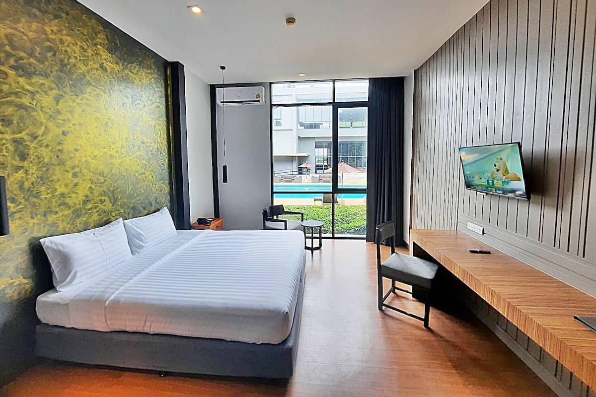 A modern hotel room with a large bed, a desk with a flat-screen TV, and a view of a swimming pool.