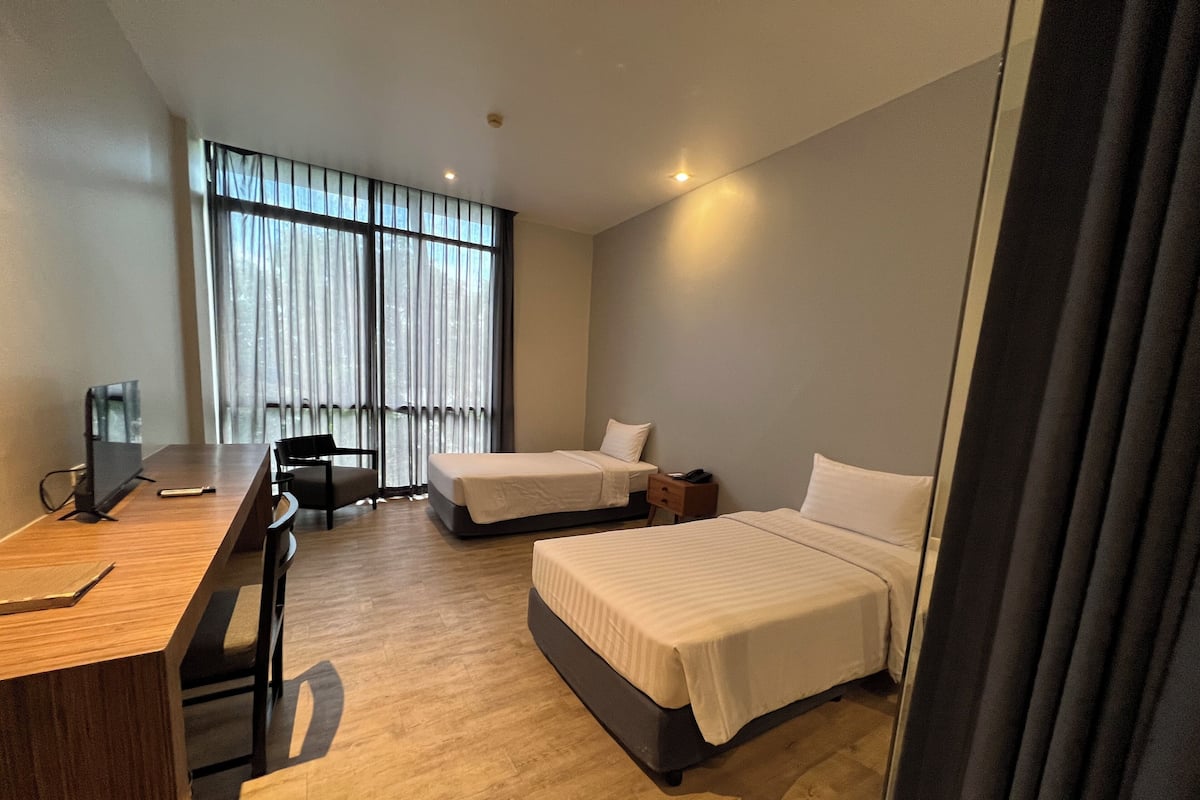 A hotel room with two beds, a desk, a chair, and a TV.