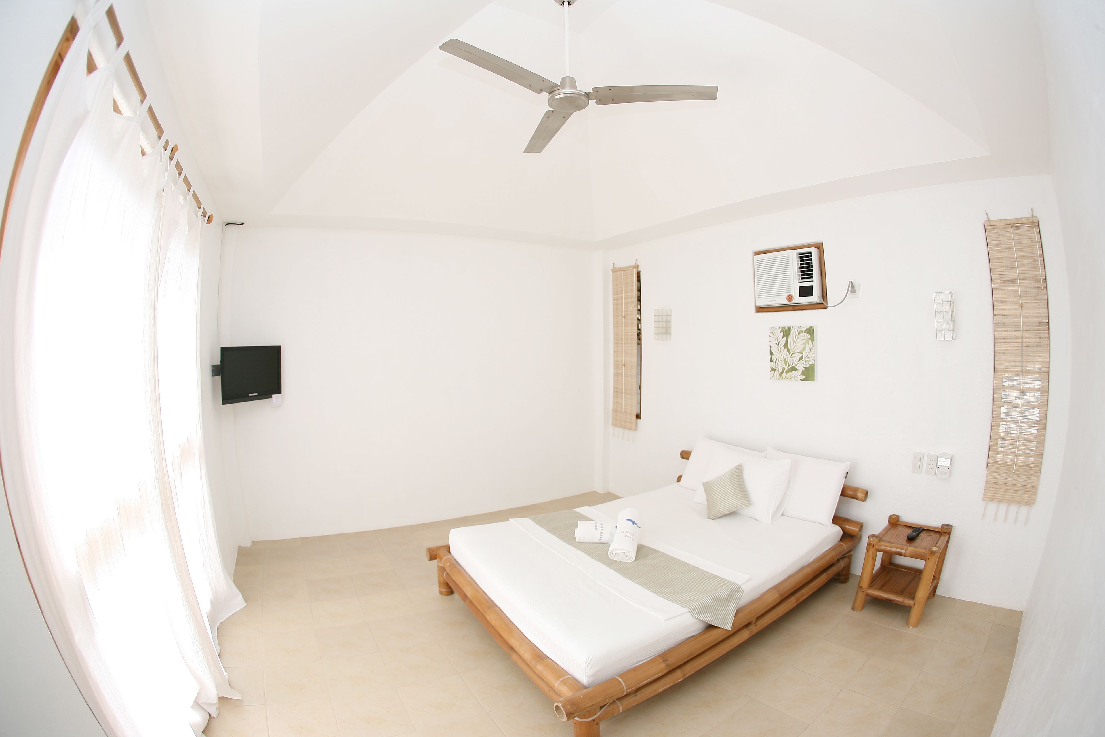 Un dormitorio con cama, ventilador de techo, unidad de aire acondicionado y una mesita de noche de madera.