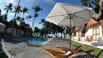 Relax by the pool surrounded by palm trees and a thatched-roof building.