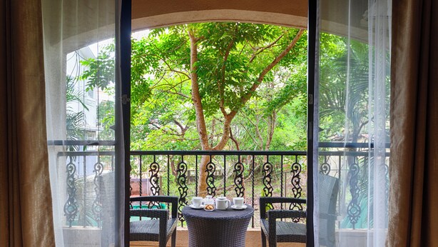 Un balcón con una mesa lista para el té, rodeado de sillas y vistas a un árbol verde y frondoso.