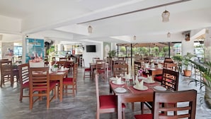 Un restaurante espacioso con mesas y sillas de madera, piso de baldosas y un amplio ventanal con vistas a un jardín.