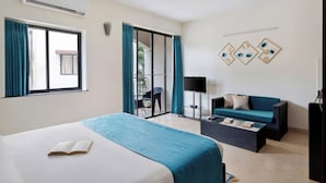 Una habitación de hotel con cama, sofá, televisión y balcón con cortinas.
