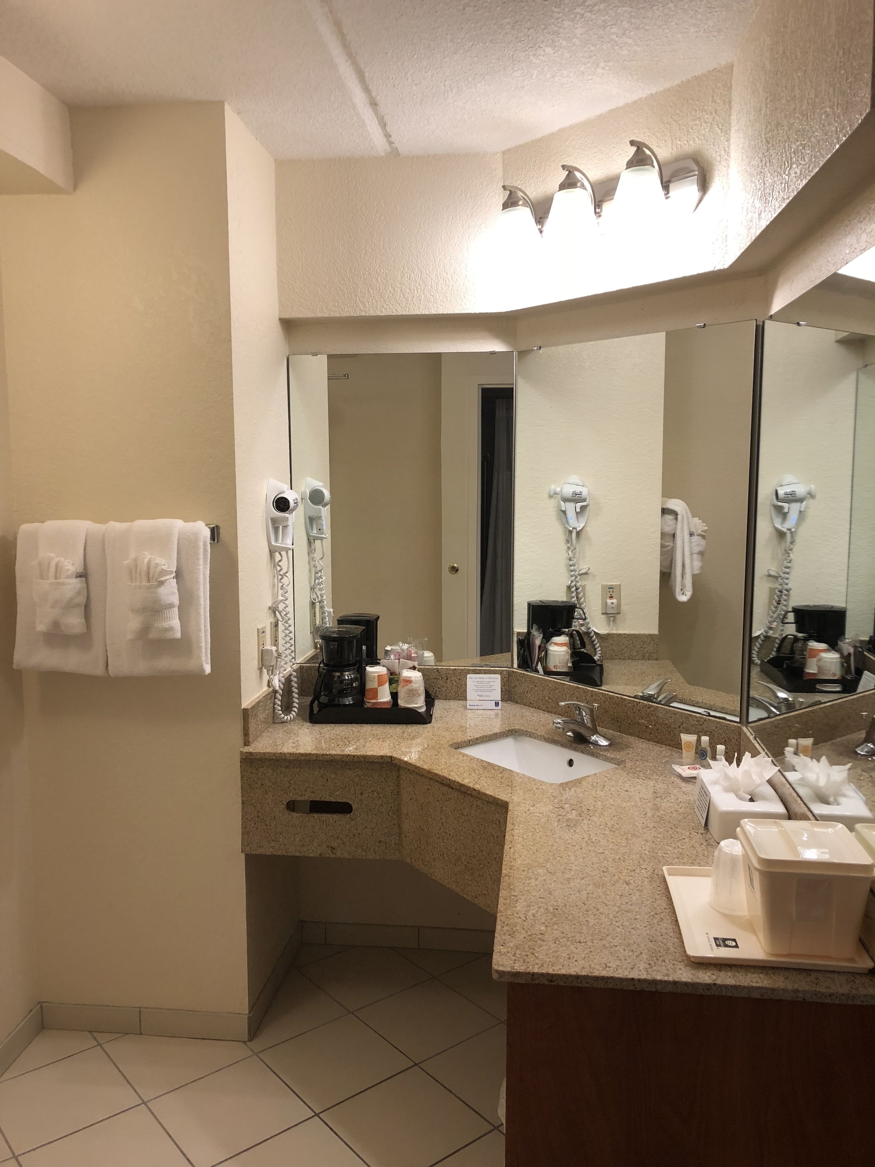 A hotel bathroom with a large mirror, a sink, a hairdryer, and a towel rack.