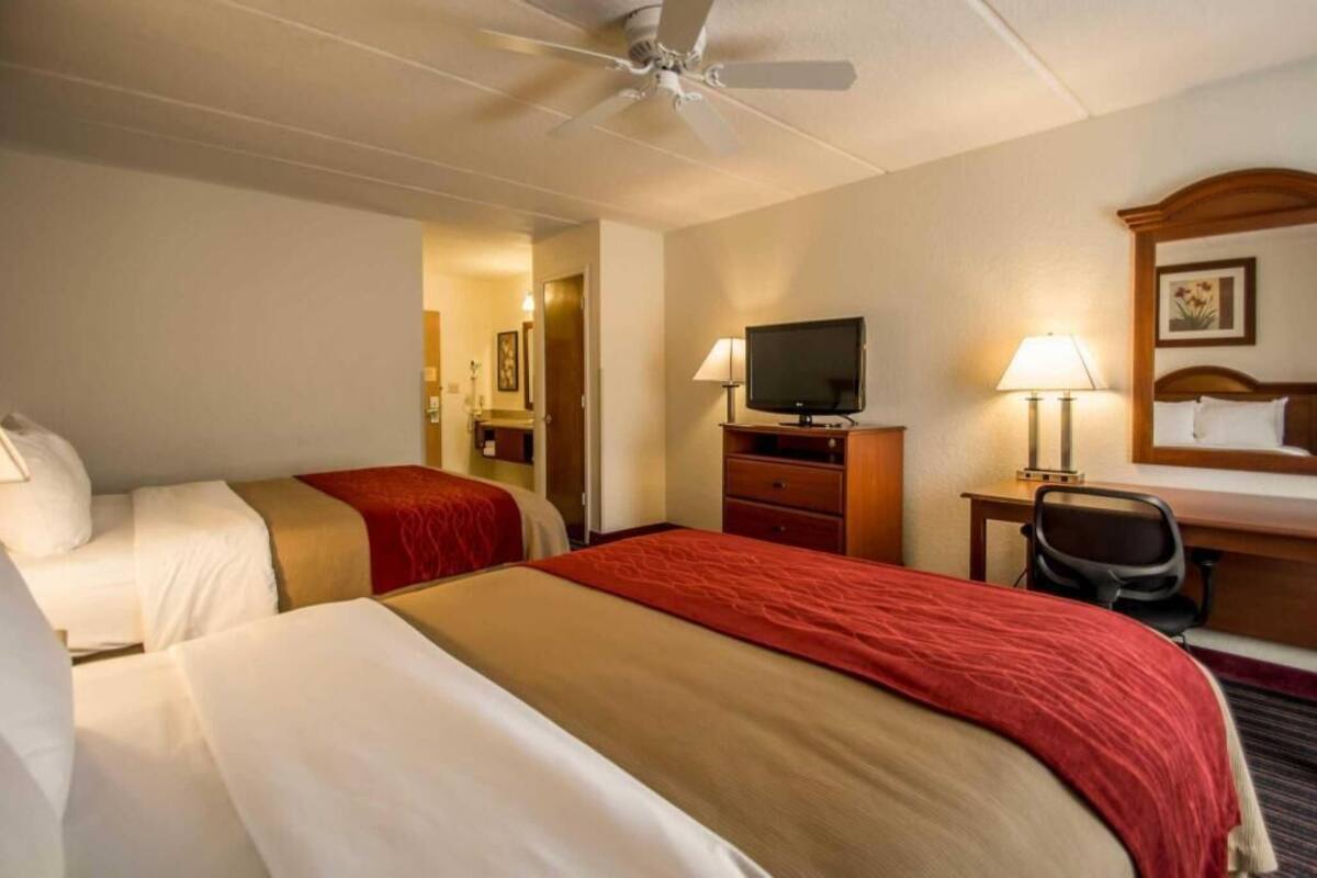 A hotel room with two beds, a television, a desk with a chair, and a ceiling fan.