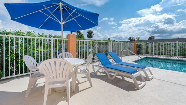 Un espace aménagé au bord de la piscine, avec des chaises blanches, une table et des fauteuils bleus placés sous un parasol bleu.