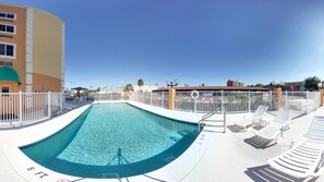 A swimming pool with a 5 ft depth marker, surrounded by white lounge chairs and a white fence.