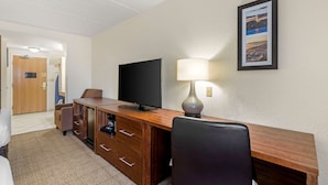 Une chambre d’hôtel avec un bureau en bois, une télévision, une lampe, un tableau encadré au mur et un lit.