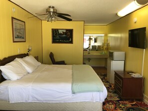 A hotel room with a bed, a desk, a chair, a mirror, a television, and a refrigerator.