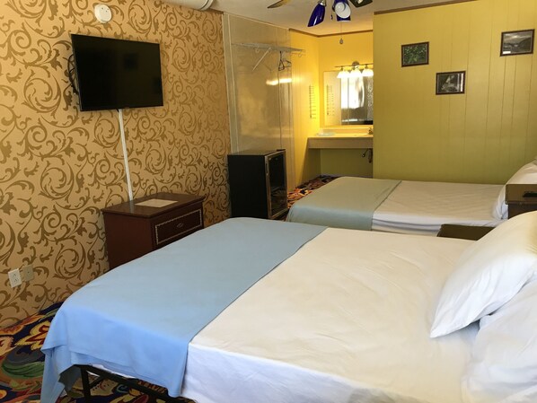 A hotel room with two beds, a TV, a mirror, and a small desk.