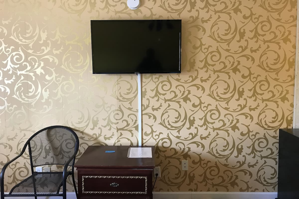Une pièce dotée d’un téléviseur à écran plat fixé au mur, d’une petite table d’appoint en bois avec une chaise, et d’un papier peint à motifs.