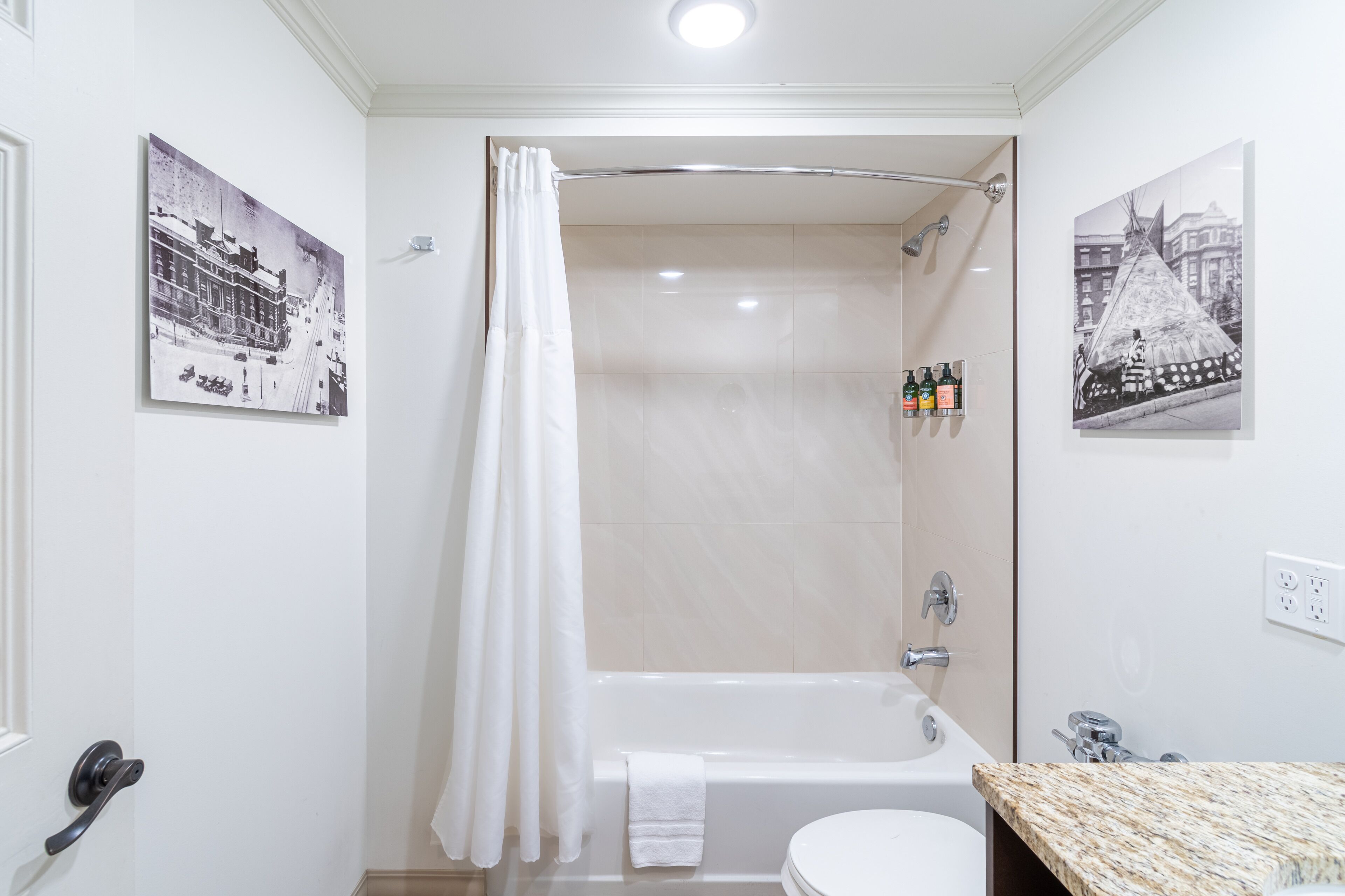 A bathroom with a bathtub, toilet, and shower curtain. There are two framed pictures on the walls.