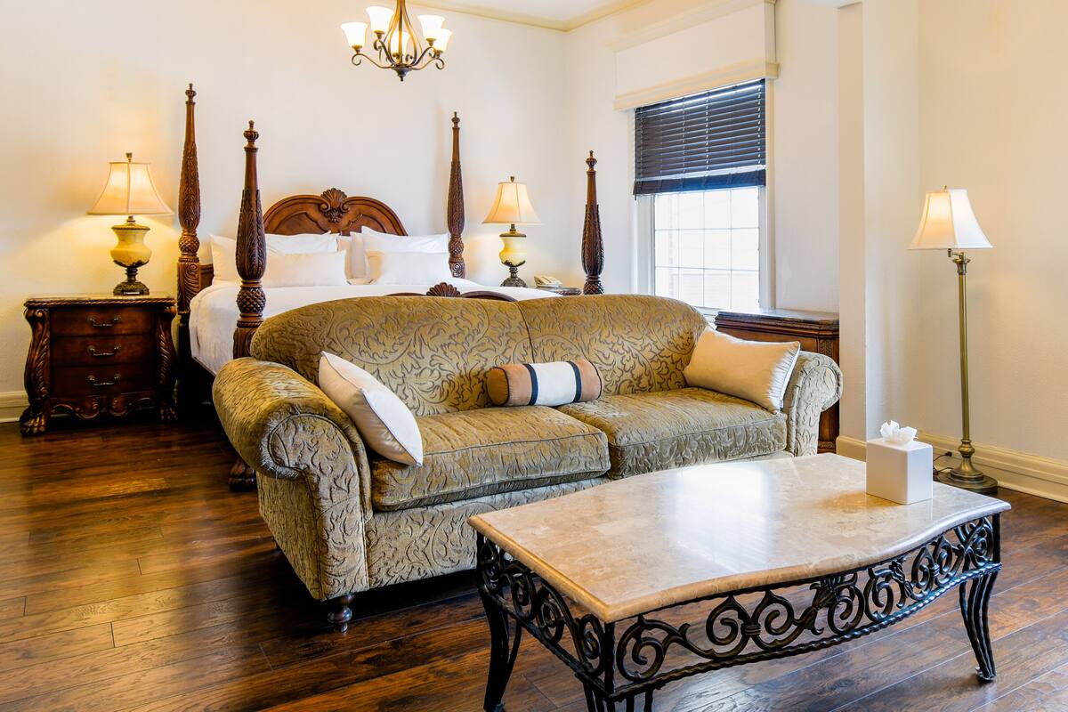 A bedroom with a four-poster bed, a sofa, a coffee table, and two bedside tables with lamps.
