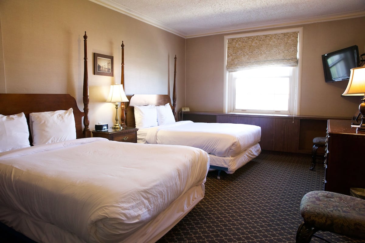 A hotel room with two beds, a television, a window with a view, and a desk with a lamp.