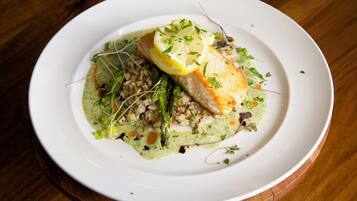 Un plato blanco con un filete de pescado, espárragos y una salsa verde sobre una mesa de madera.