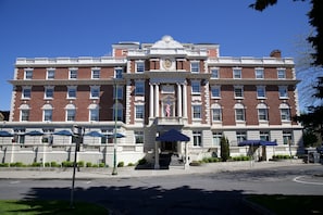A large, historic building with a symmetrical facade, multiple windows, and a central entrance with a flag.