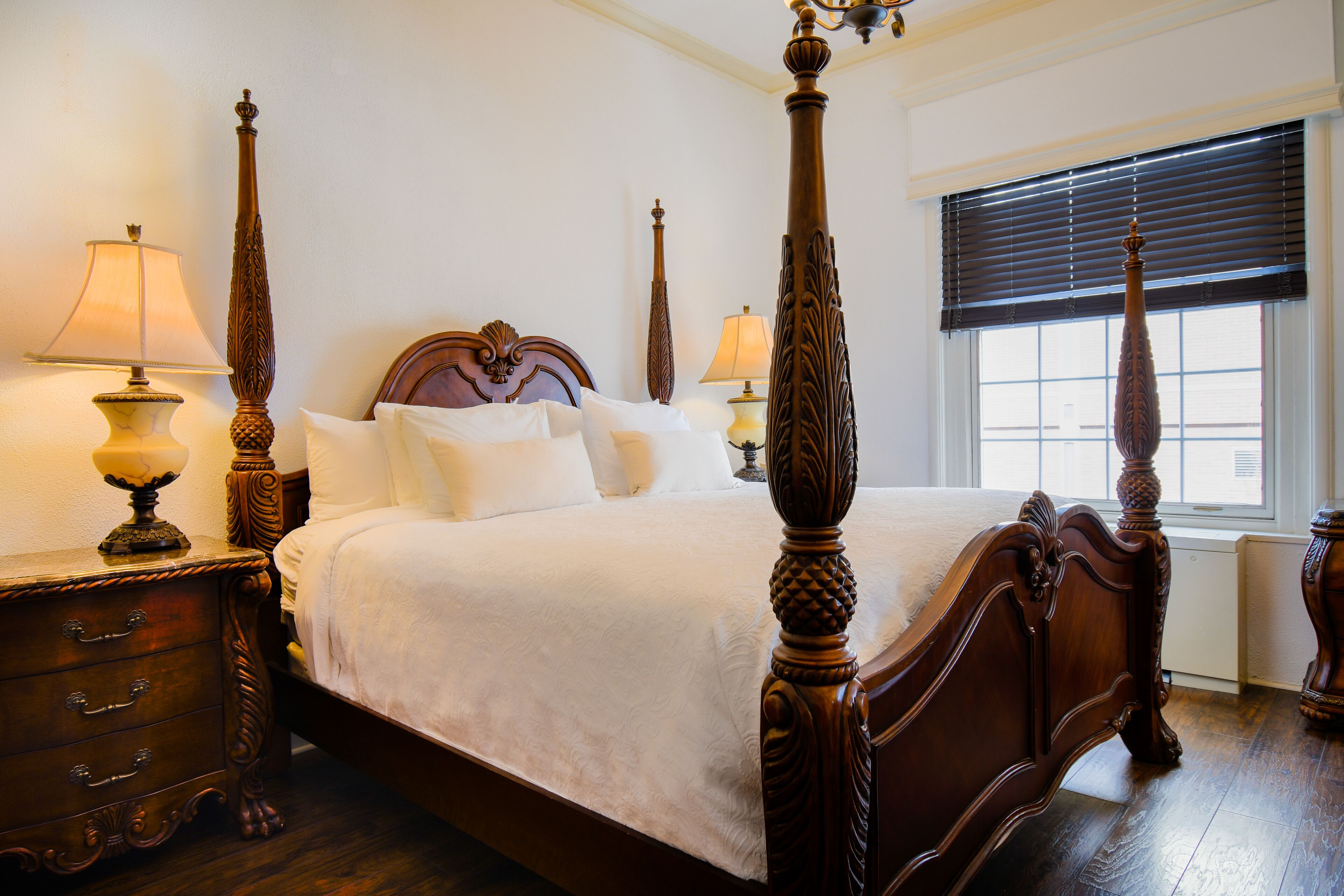 A four-poster bed with ornate wooden posts and a matching headboard, flanked by two nightstands with lamps.
