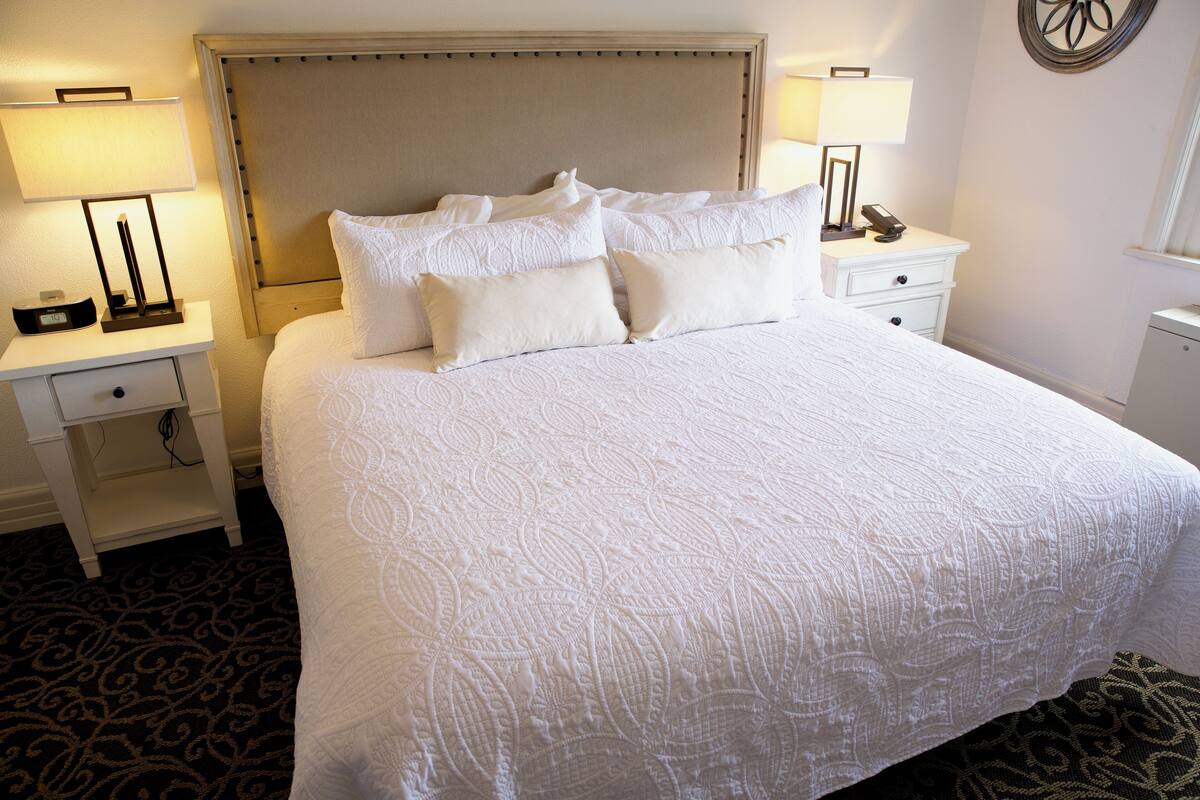 A neatly made bed with a patterned bedspread, two bedside tables with lamps, and a wall-mounted decorative item.