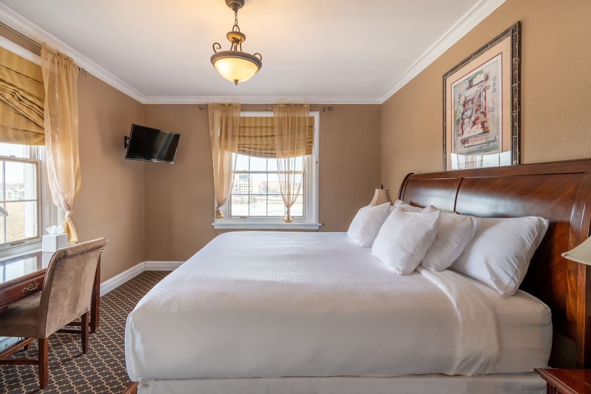 A hotel room with a large bed, a desk, a television, and a window with curtains.