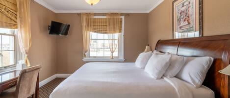 A hotel room with a large bed, a desk, a television, and a window with curtains.