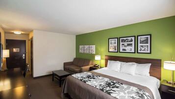 Habitación de hotel con cama, sofá, escritorio y mesita de noche. En la pared hay cuadros enmarcados y una puerta al fondo.