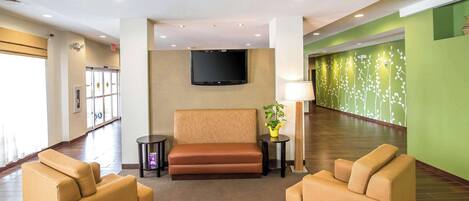 Un hall con un sofá, dos sillones, un televisor, una lámpara y una planta.
