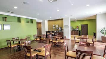 A spacious dining area with multiple tables and chairs, a kitchen in the background, and green walls.