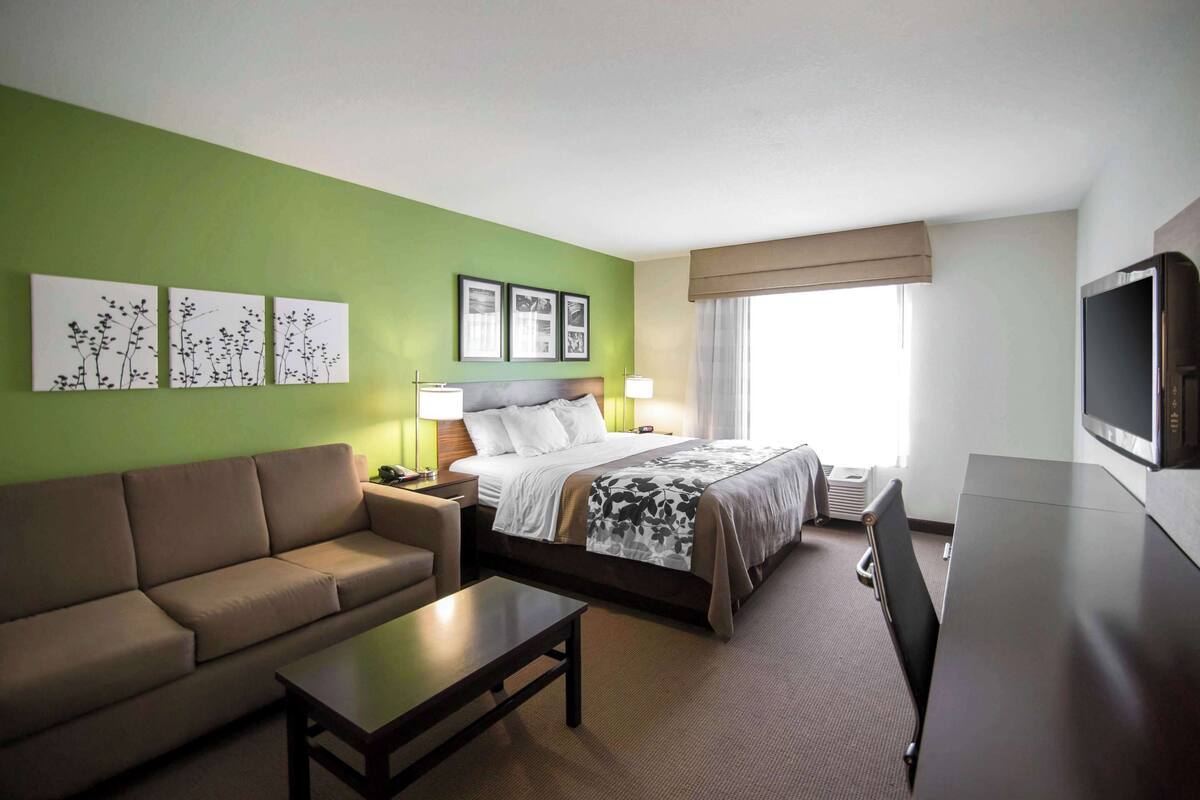 A hotel room with a bed, a sofa, a coffee table, and a TV.