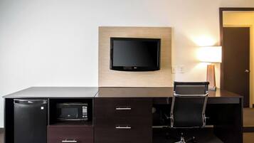 A hotel room with a dark wooden desk, a flat-screen TV mounted on the wall, a microwave, and a chair.