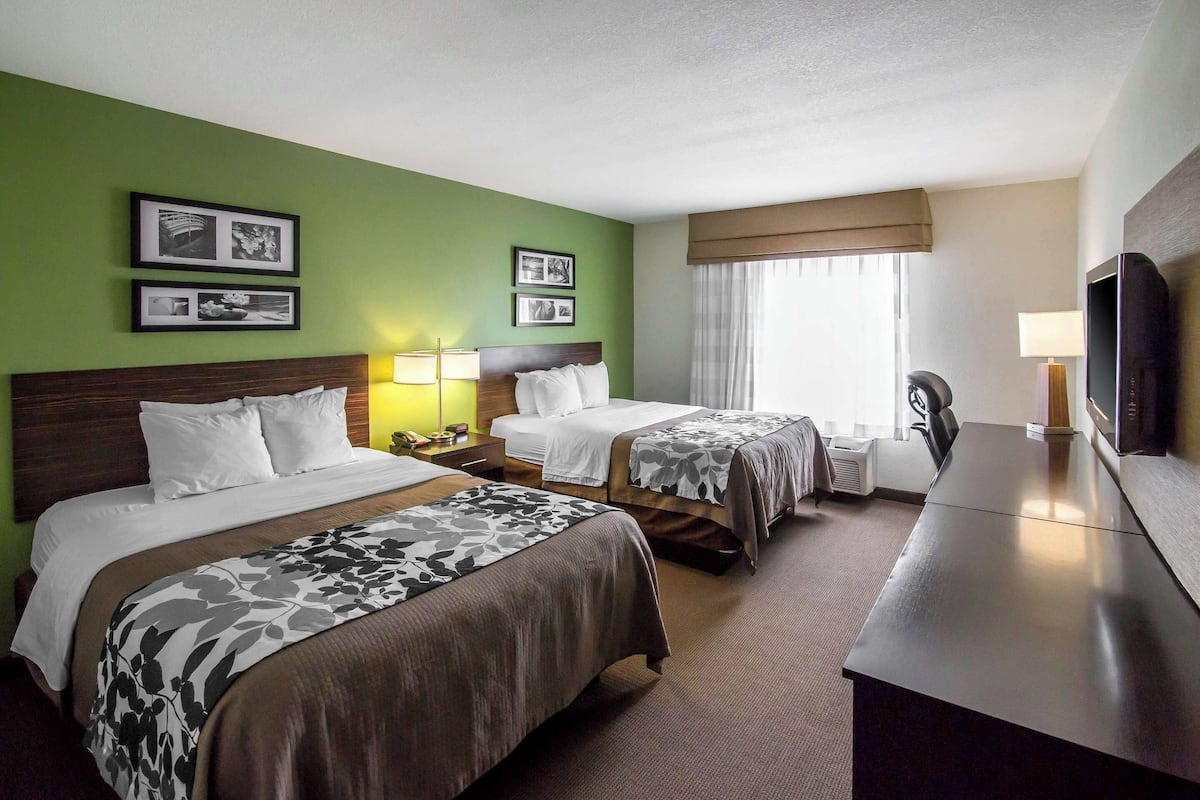 A hotel room with two beds, a desk, and a television.